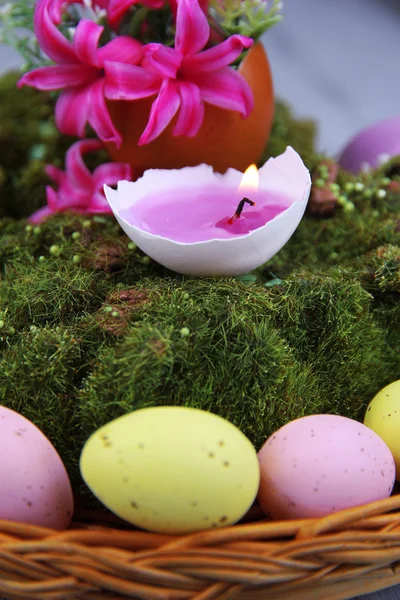 Composition conceptuelle de Pâques. Bougie brûlante dans l'oeuf, oeufs de Pâques, et des fleurs sur la mousse décorative et tapis d'osier, sur fond en bois, gros plan — Photo