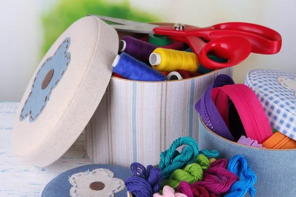 Decorative boxes with colorful skeins of thread and zippers on table on bright background — Stock Photo, Image