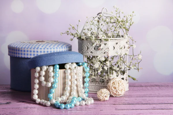 Decorative boxes with beads and flowers on table on bright background — Stock Photo, Image