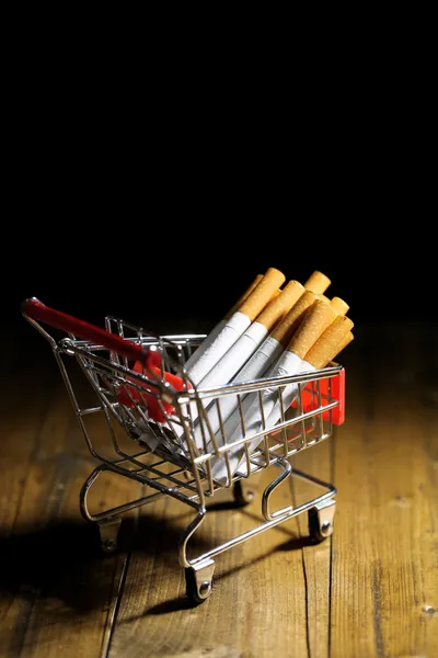 Sigaretten in winkelwagen op houten tafel op donkere achtergrond — Stockfoto