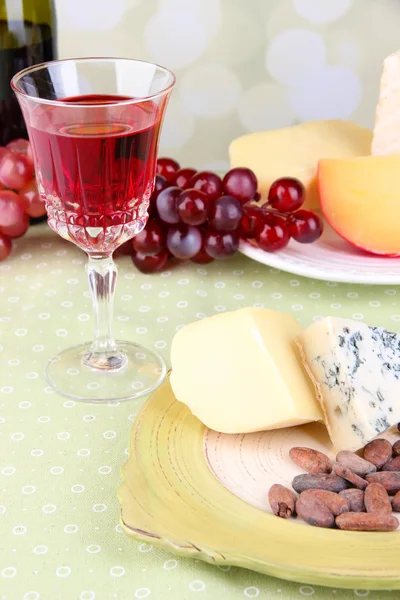 Placa de queso surtido, copa de uva y vino en la mesa, sobre fondo claro — Foto de Stock