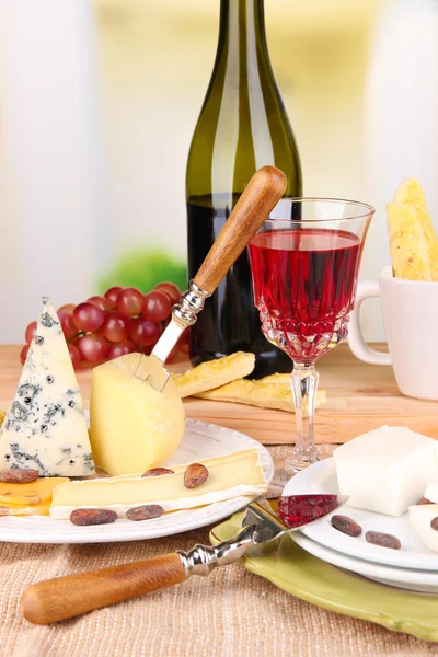 Placa de queso surtido, copa de uva y vino en la mesa, sobre fondo claro —  Fotos de Stock