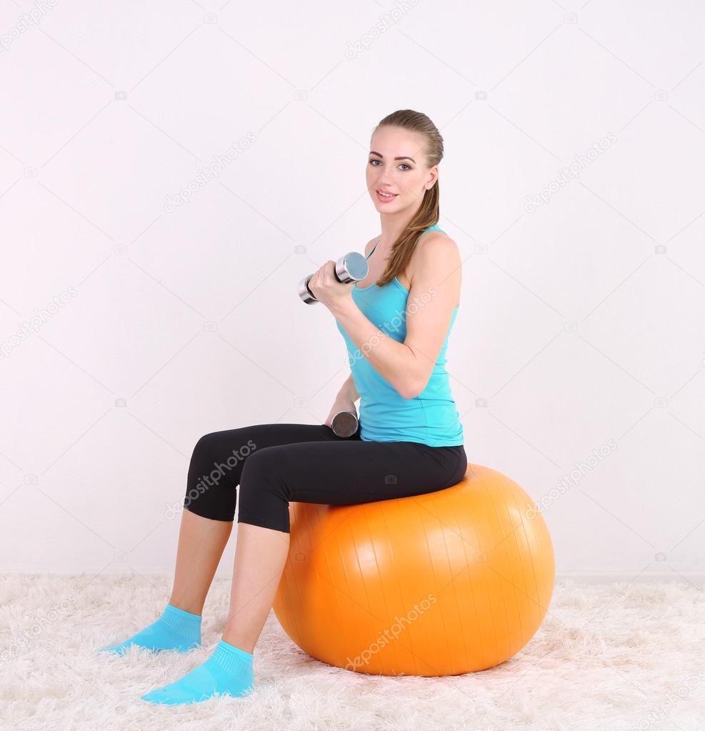 Young beautiful fitness girl exercising with orange ball and dumbbells in gym