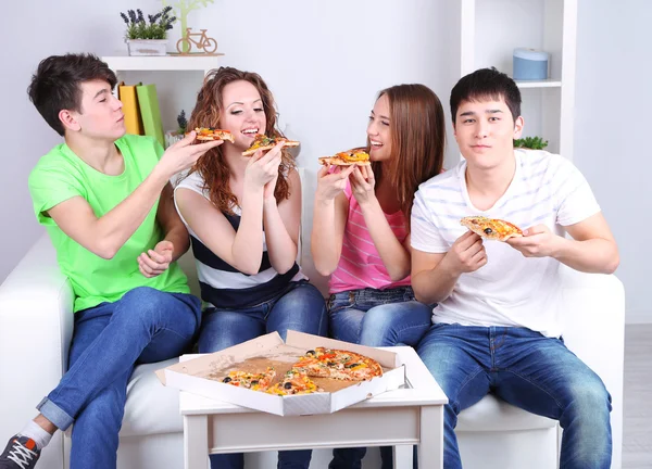 Groupe de jeunes amis mangeant de la pizza dans le salon sur le canapé — Photo