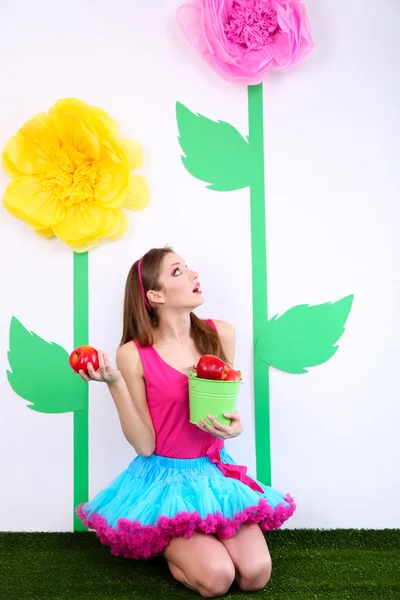 Beautiful young woman in petty skirt holding bucket of apples on decorative background — Stock Photo, Image