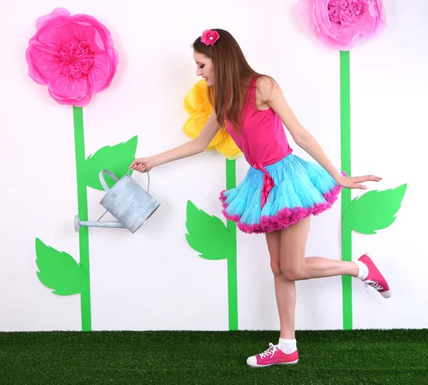 Beautiful young woman in petty skirt watering flower on decorative background — Stock Photo, Image