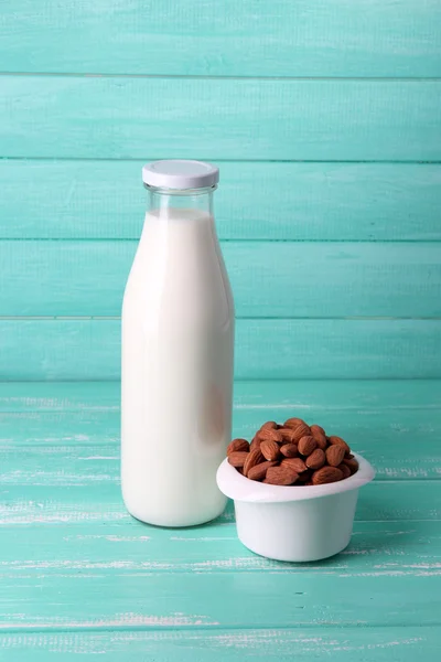 Mandlové mléko v lahvi s mandlemi v míse, na barevné dřevěné pozadí — Stock fotografie