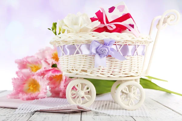 Beautiful tulips and gift box in decorative wicker basket, on wooden table, on light background — Stock Photo, Image