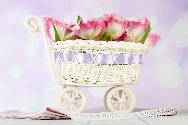 Красивые тюльпаны в декоративной плетеной корзине, на деревянном столе, на светлом фоне — стоковое фото