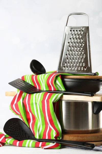 Stacked cooking equipment on wooden table, on light background — Stock Photo, Image