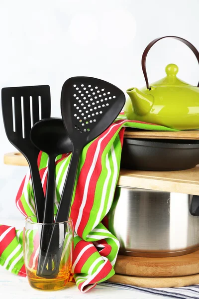 Stacked cooking equipment on wooden table, on light background — Stock Photo, Image