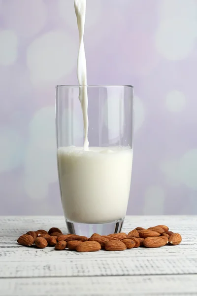 Mandelmilch wird in Glas gegossen, auf farbigem Holztisch, auf hellem Hintergrund — Stockfoto