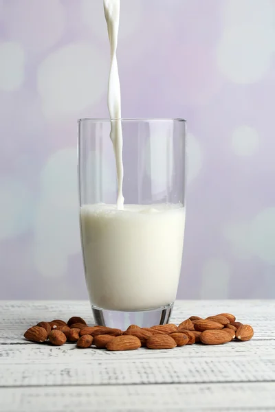 Le lait d'amande est versé dans du verre, sur une table en bois de couleur, sur un fond clair — Photo