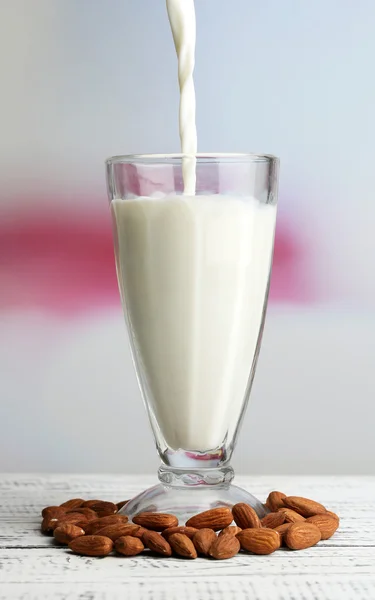 Susu almond dituangkan ke dalam gelas, di atas meja kayu berwarna, di latar belakang cahaya — Stok Foto