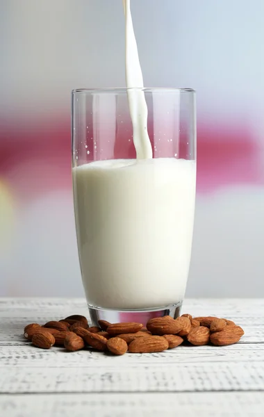 Миндальное молоко наливают в стекло, на цветной деревянный стол, на светлый фон — стоковое фото
