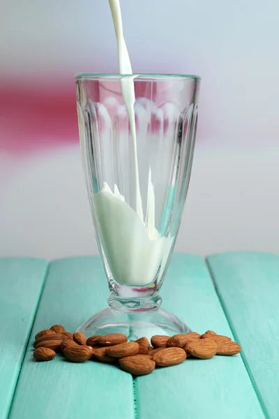 La leche de almendras se vierte en vidrio, sobre una mesa de madera de color, sobre un fondo claro — Foto de Stock