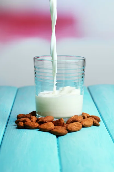 Susu almond dituangkan ke dalam gelas, di atas meja kayu berwarna, di latar belakang cahaya — Stok Foto