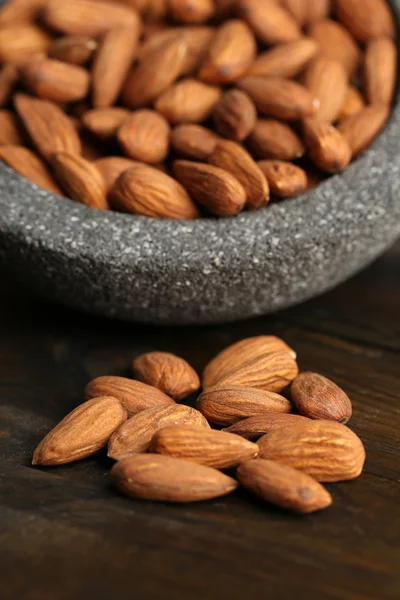 Almonds in bowl on color wooden background — Stock Photo, Image