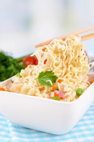 Νόστιμο στιγμιαία noodles με λαχανικά σε μπολ στο τραπέζι επάνω ελαφρύς υπόβαθρο — Φωτογραφία Αρχείου