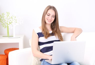 Evdeki kanepede dizüstü bilgisayarıyla dinlenen genç bir kadın.