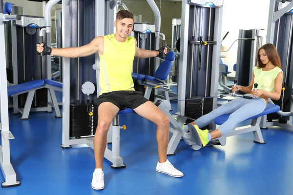 Chico y chica involucrados en simulador en el gimnasio —  Fotos de Stock