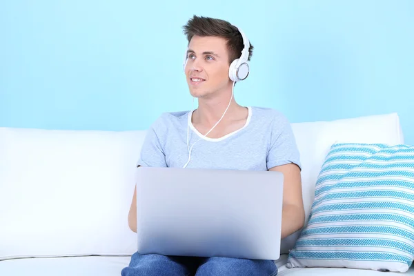 Facet siedzi na kanapie i słuchanie muzyki na niebieskim tle — Zdjęcie stockowe