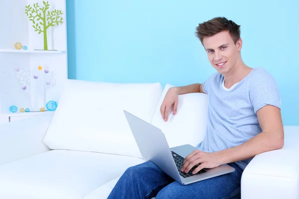 Cara sentado no sofá com laptop no fundo azul — Fotografia de Stock