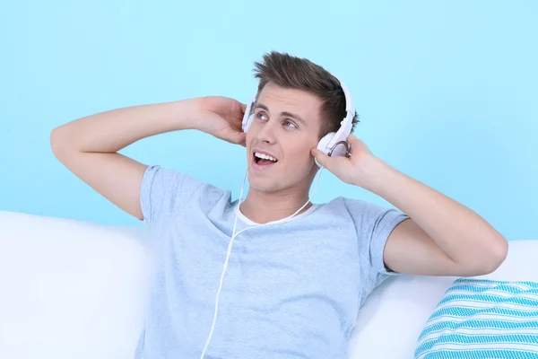 Chico sentado en el sofá y escuchando música sobre fondo azul —  Fotos de Stock