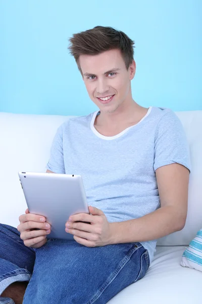 Guy assis sur un canapé avec tablette électronique sur fond bleu — Photo