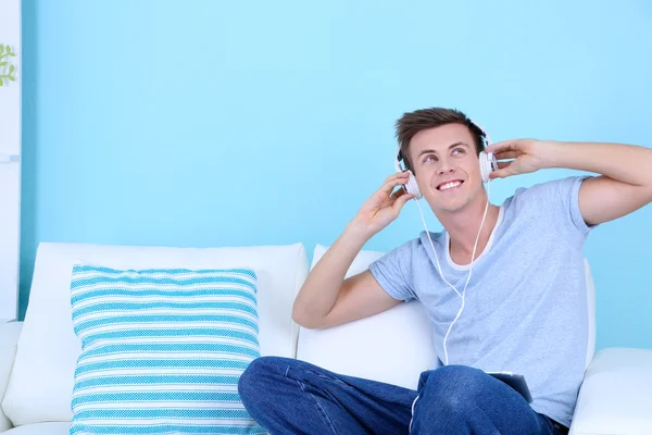 Chico sentado en el sofá y escuchando música sobre fondo azul — Foto de Stock