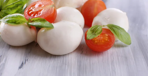 Tasty mozzarella cheese with basil and tomatoes, on wooden table — Stock Photo, Image