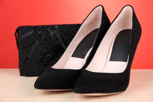 Sapatos femininos pretos bonitos e saco no fundo vermelho — Fotografia de Stock