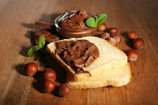 Pain avec tartinade de noisettes au chocolat sucré sur fond en bois — Photo