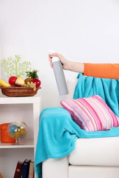 Sprayed air freshener in hand on home interior background — Stock Photo, Image