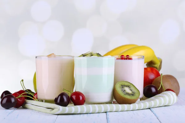 Delizioso yogurt con gusti di frutta in bicchieri e frutta fresca su tovagliolo, su sfondo chiaro — Foto Stock