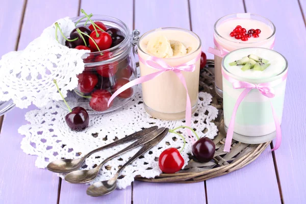 Delicious yogurt with fruits tastes in glasses and fresh fruits on color wooden background — Stock Photo, Image