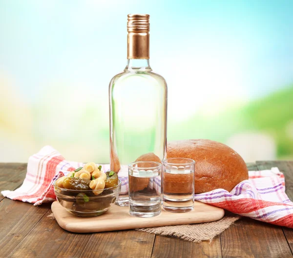 Composition with bottle of vodka and marinated vegetables on wooden table, on bright background — Stock Photo, Image