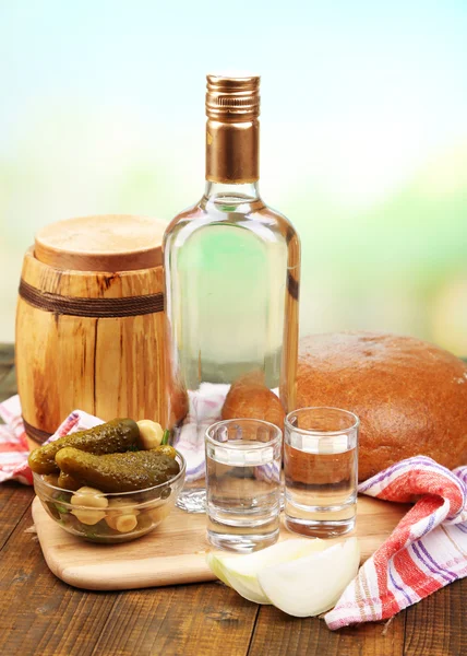 Composição com garrafa de vodka e legumes marinados na mesa de madeira, no fundo brilhante — Fotografia de Stock