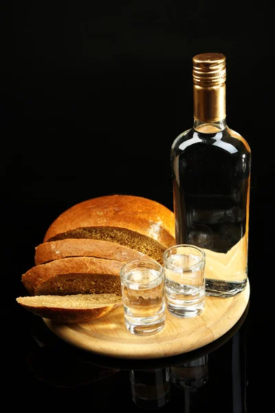 Láhev vodky, čerstvý chléb a brýle na dřevěné desce, izolované na černém pozadí — Stock fotografie