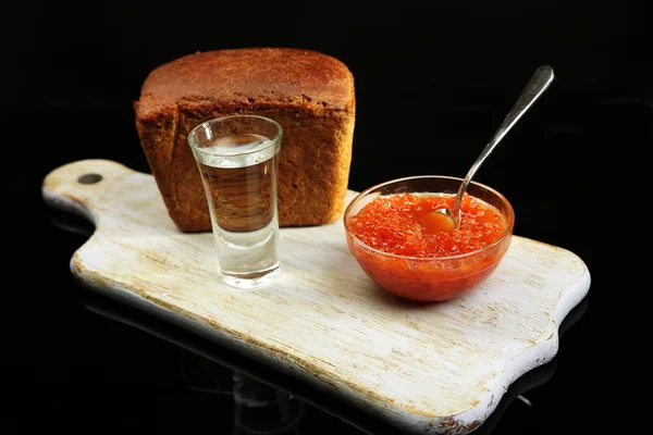 Composición con vaso de vodka, caviar rojo, pan fresco sobre tabla de madera, aislado sobre negro —  Fotos de Stock