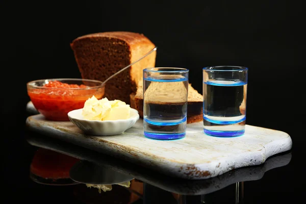 Composición con vasos de vodka, caviar rojo, pan fresco sobre tabla de madera, aislado sobre negro —  Fotos de Stock