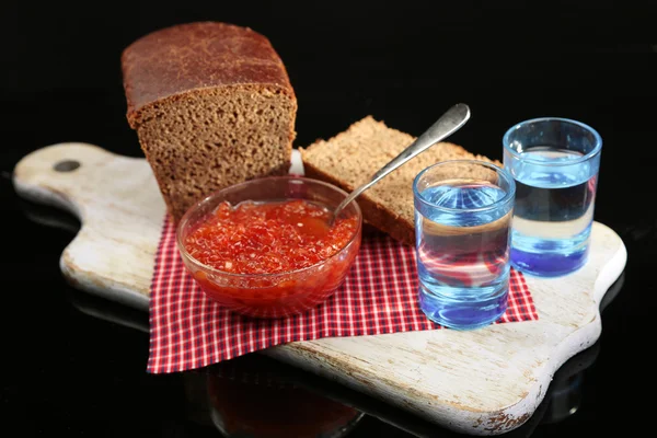 Composición con vasos de vodka, caviar rojo, pan fresco sobre tabla de madera, aislado sobre negro —  Fotos de Stock