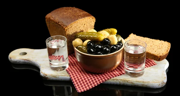 Состав со стаканами водки и маринованными овощами, свежий хлеб на деревянной доске, изолированный на черном — стоковое фото