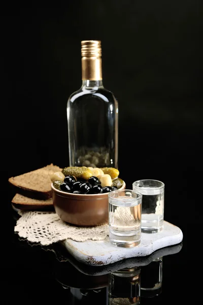 Kompozycja z butelką wódki i marynowane warzywa, świeże pieczywo na desce, na czarnym tle — Zdjęcie stockowe