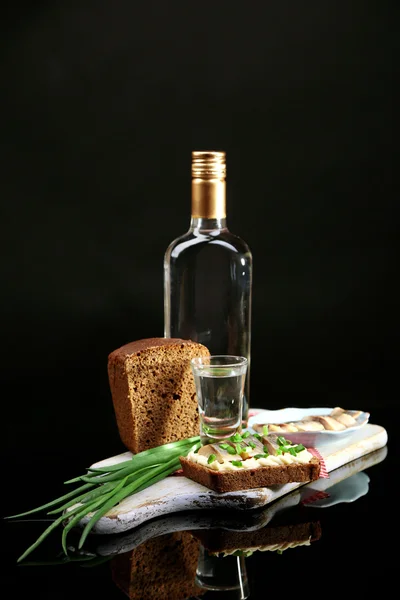 Composición con botella de vodka, sándwich con pescado salado, cebolla verde y vidrio sobre tabla de madera, aislado sobre negro —  Fotos de Stock