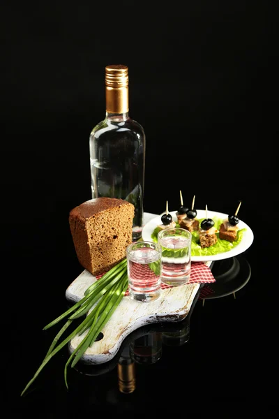 Složení s lahví vodky, občerstvení s solené ryby, zelené cibulky a skla na dřevěné desce, izolované na černém pozadí — Stock fotografie
