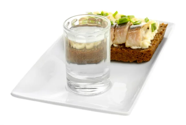 Composição com copo de vodka, e sanduíches com peixe salgado, isolado em branco — Fotografia de Stock