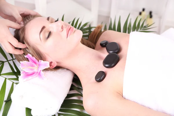 Piękna młoda kobieta o masażu głowy i kamień w salonie spa — Zdjęcie stockowe