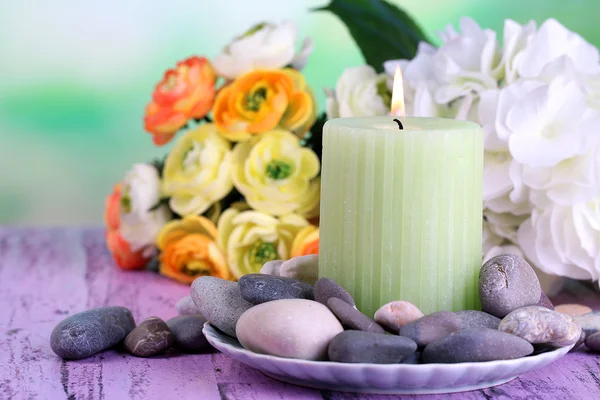 Композиція з спа-кам'яними, свічками та квітами на кольоровому дерев'яному столі, на світлому фоні — стокове фото