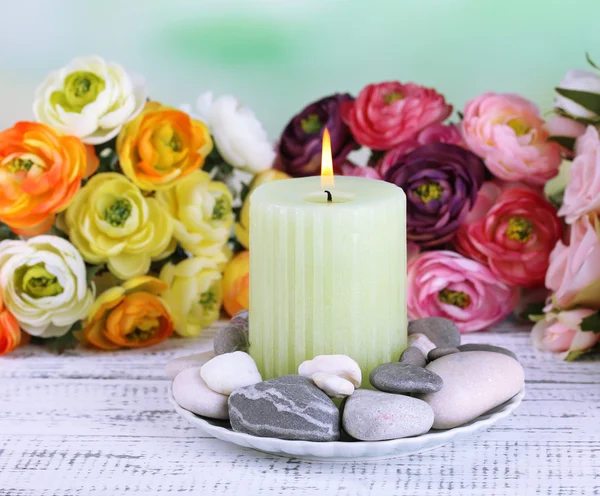 Composição com pedras de spa, vela e flores na mesa de madeira cor, no fundo claro — Fotografia de Stock